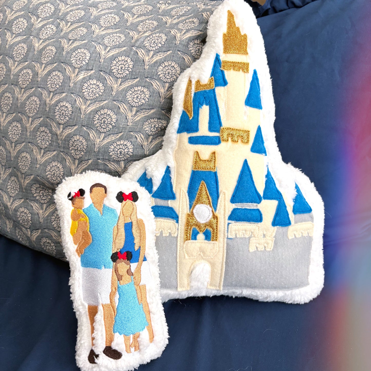 Decorative plush with castle design and people on a blue comforter on bed.
