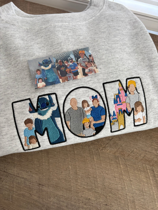 Grey sweatshirt with embroidered designs of people in various poses on a wooden surface.