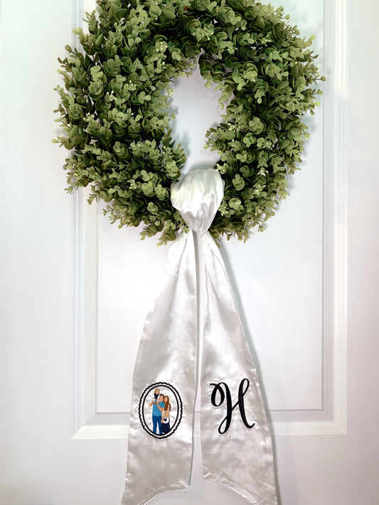 Green wreath with a white ribbon featuring a monogram on a white door.
