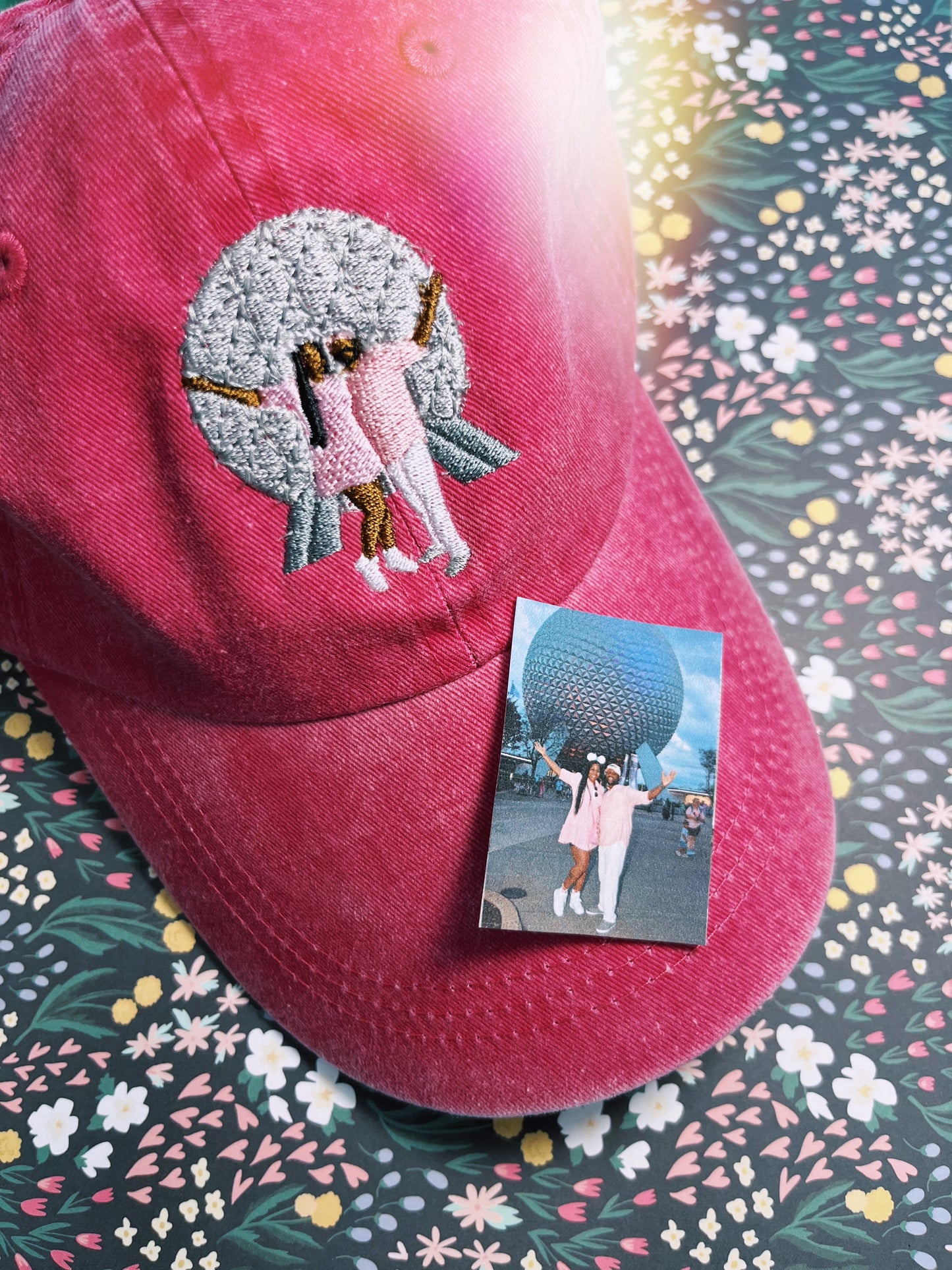 Embroidery design of a ball, with two people standing in front of it on a hat.