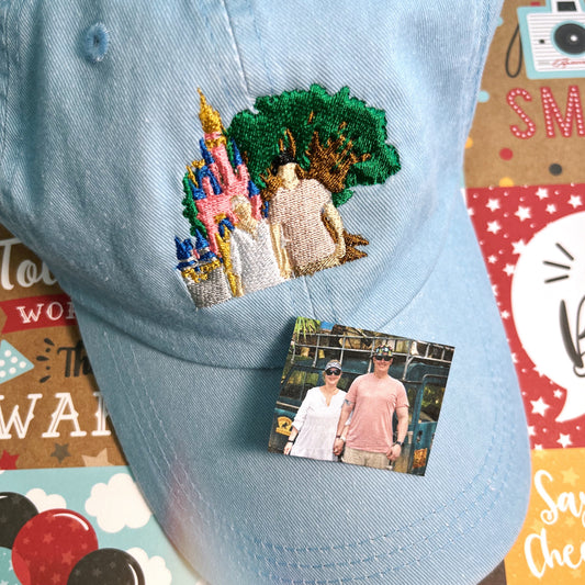 Blue hat that has an embroidered design of a tree and castle with two people.