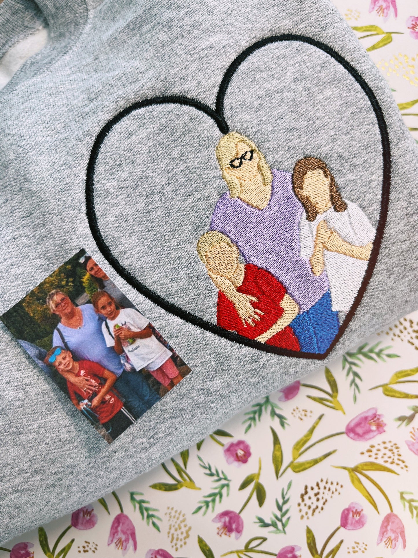 Grey sweatshirt with an embroidered heart. Heart is filled with a photo submission embroidery of three people.