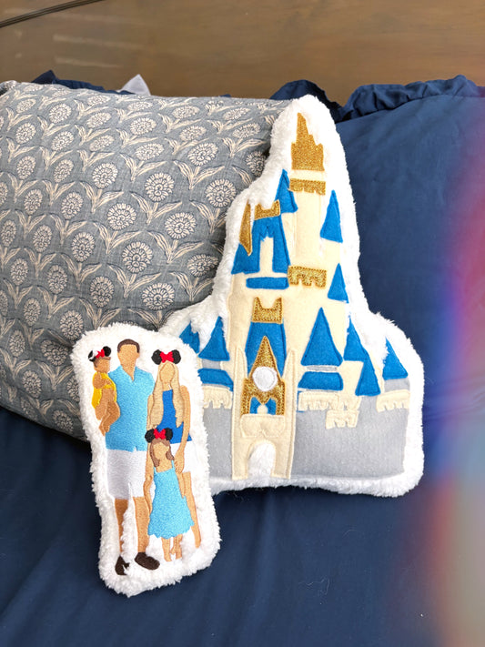Decorative plush with castle design and people on a blue comforter on bed.