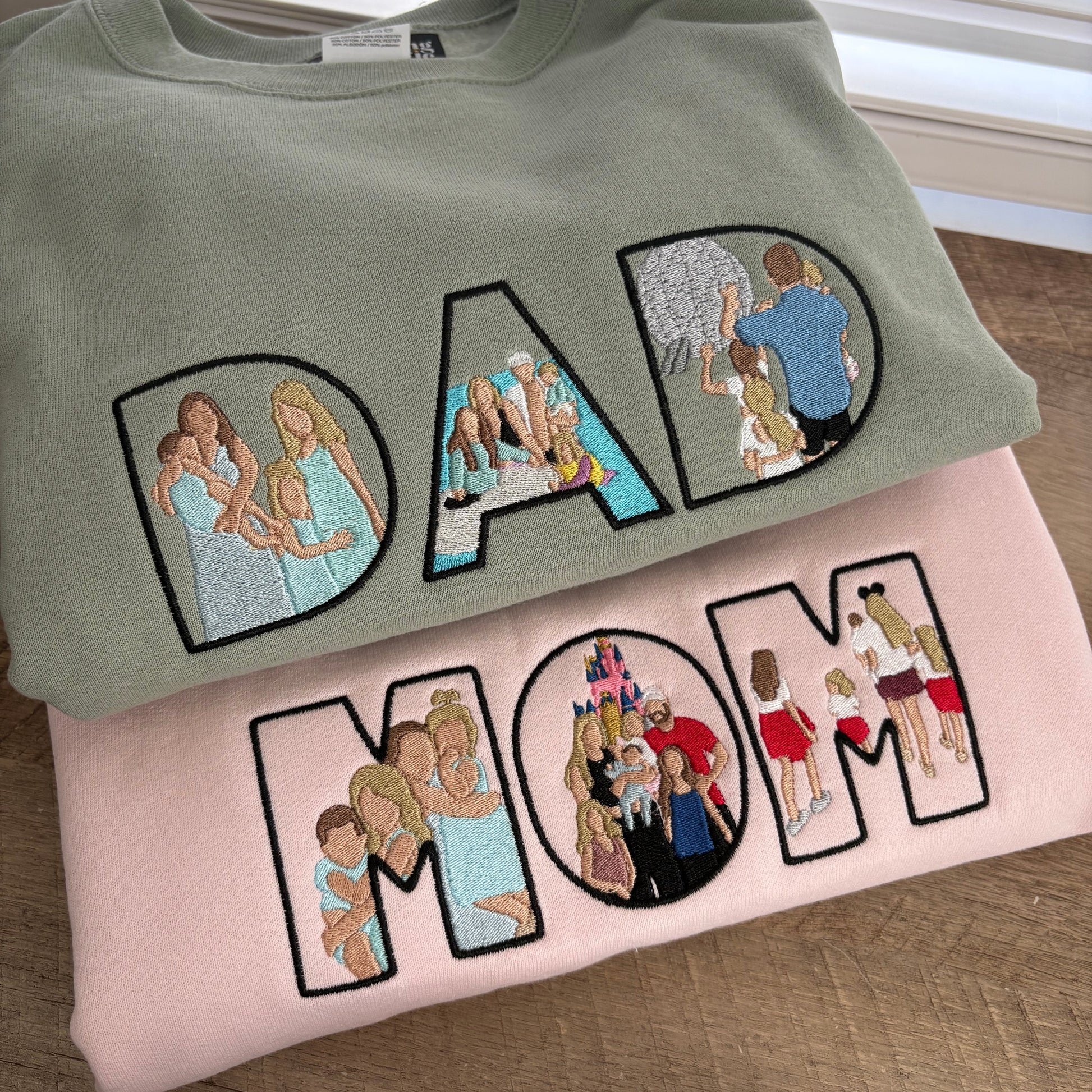 Two sweatshirts with embroidered designs of a family on a wooden surface.