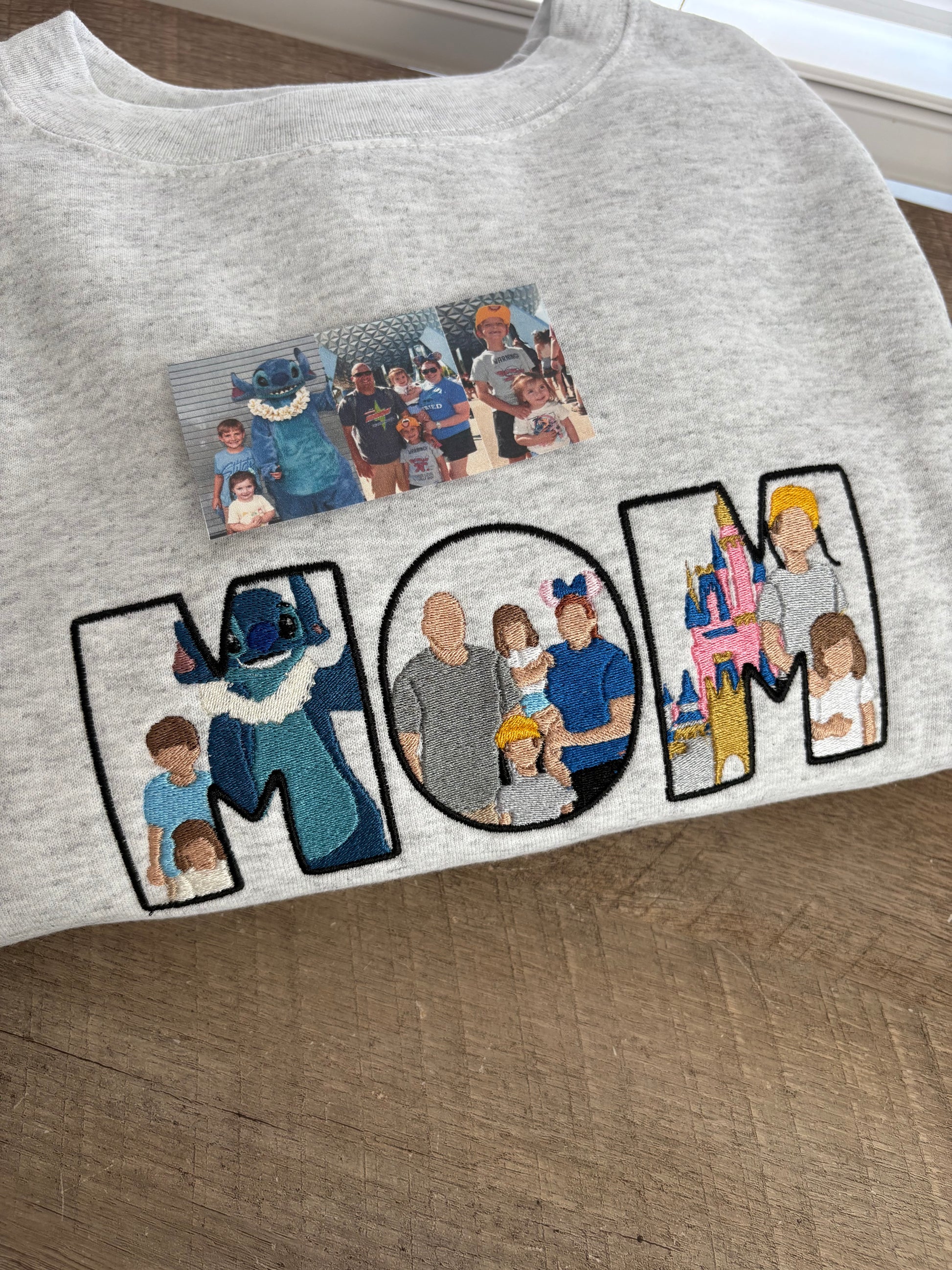 Grey sweatshirt with embroidered designs of people in various poses on a wooden surface.