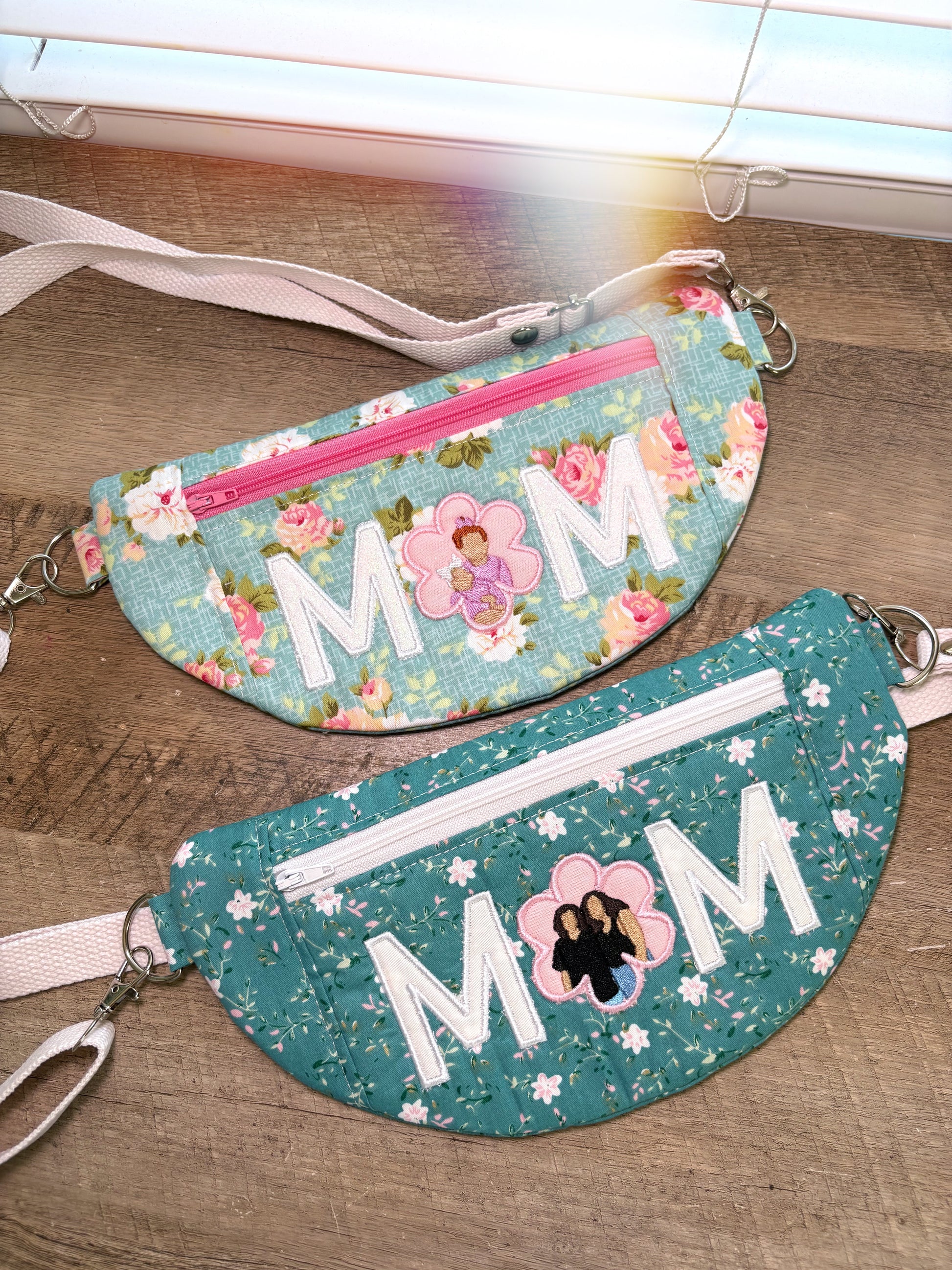 Two floral-patterned fanny packs with 'MOM' text on a wooden surface.