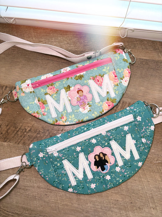 Two floral-patterned fanny packs with 'MOM' text on a wooden surface.