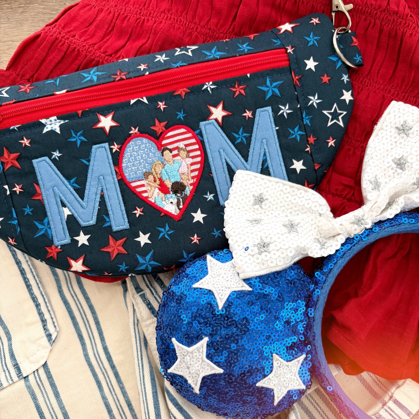 Red shirt and striped shorts in the background with character headband and star crossbody bag with MOM embroidered. 