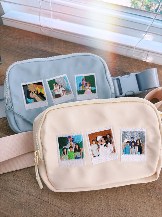 Two Fanny packs. One is blue with embroidery and the other one on top of it is cream with embroidery.