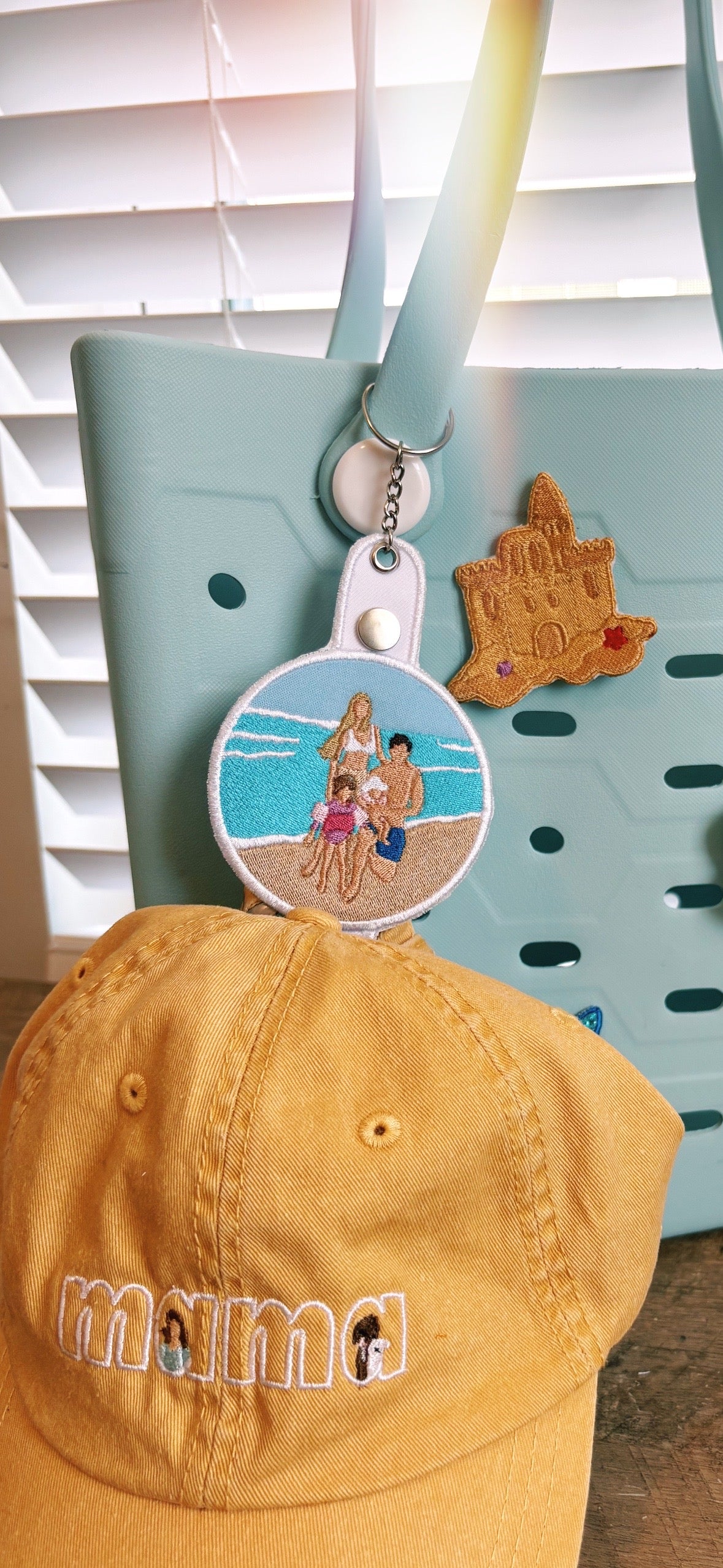 Yellow cap with 'mama' embroidery, blue bag, and beach-themed keychain with sandcastle design.