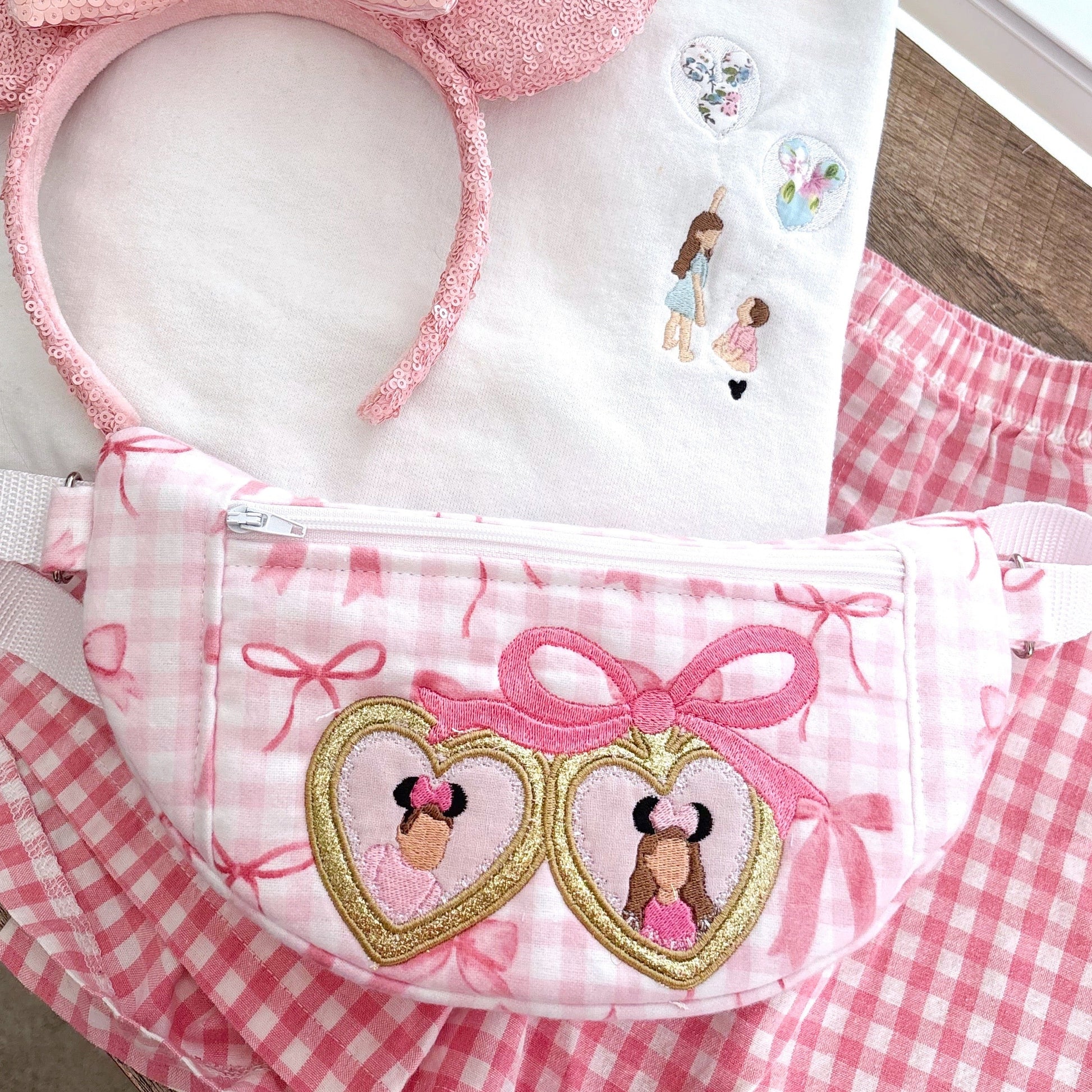 Pink and white checkered crossbody with embroidered designs on a wooden surface.