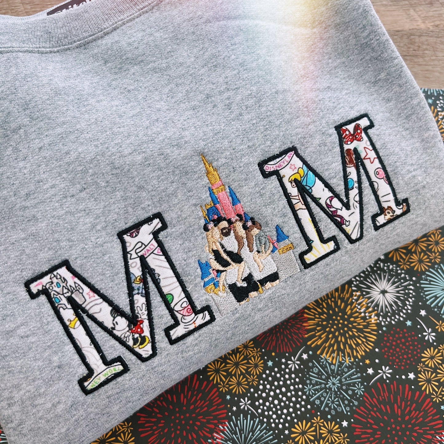 Gray sweatshirt with 'MOM' design featuring a castle and family on a firework background.