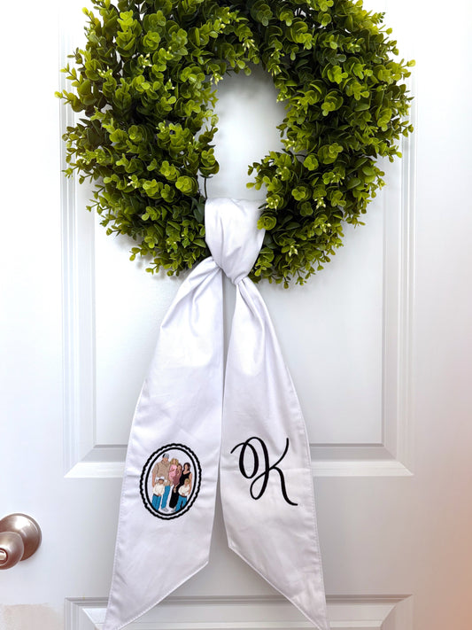 Green wreath on a white door with a white scarf featuring a couple's photo and initials.