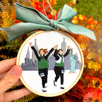 Fall floral background with a custom embroidered ornament of two girls running and a blue now on top.